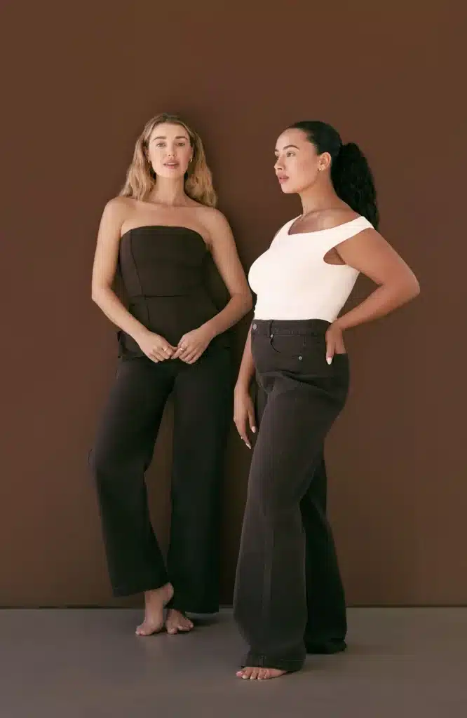Two women modeling dark brown wide-leg jeans with a matching strapless top and a white off-the-shoulder top