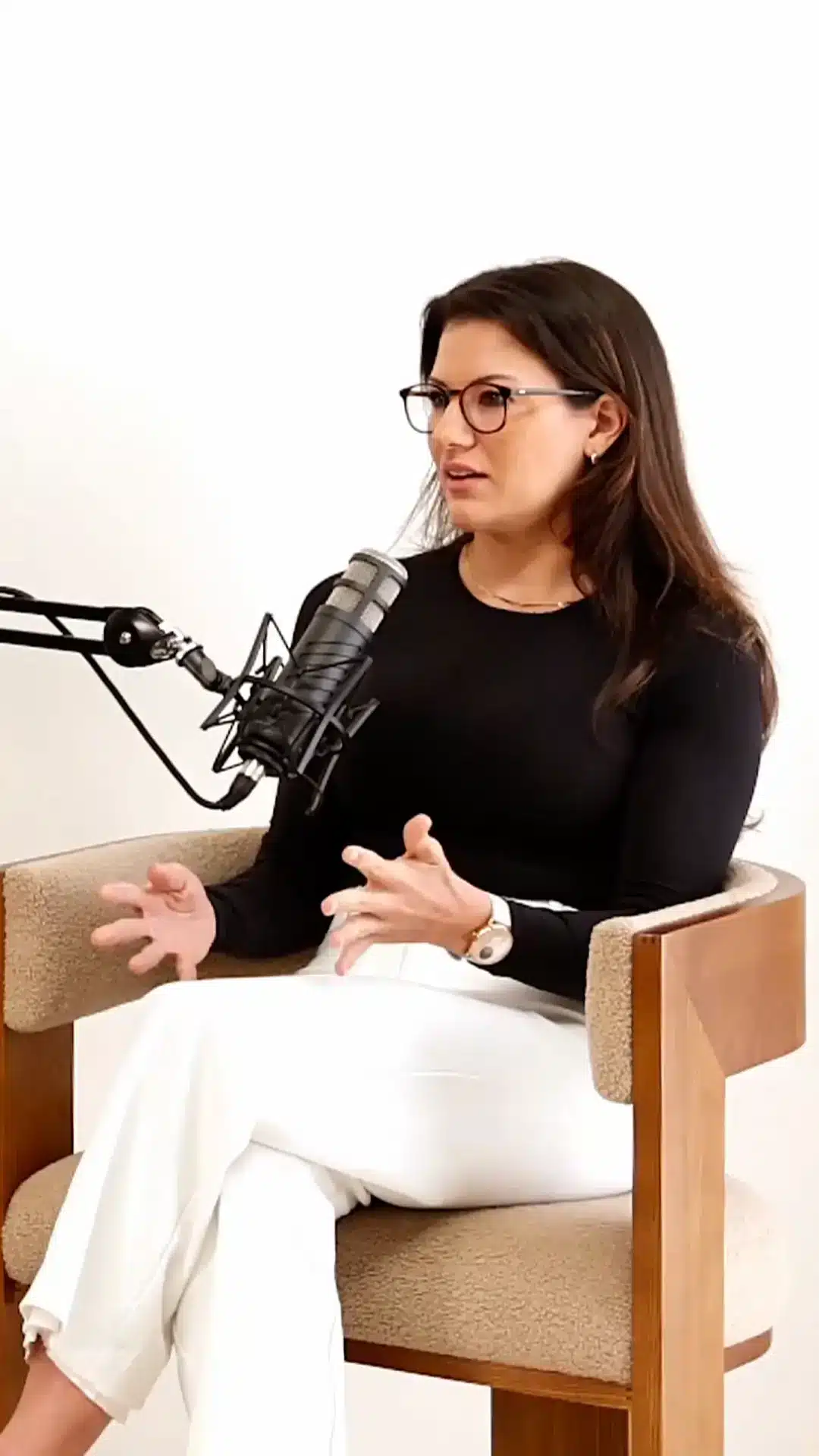 Woman with glasses sitting in an armchair, gesturing as she speaks into a microphone