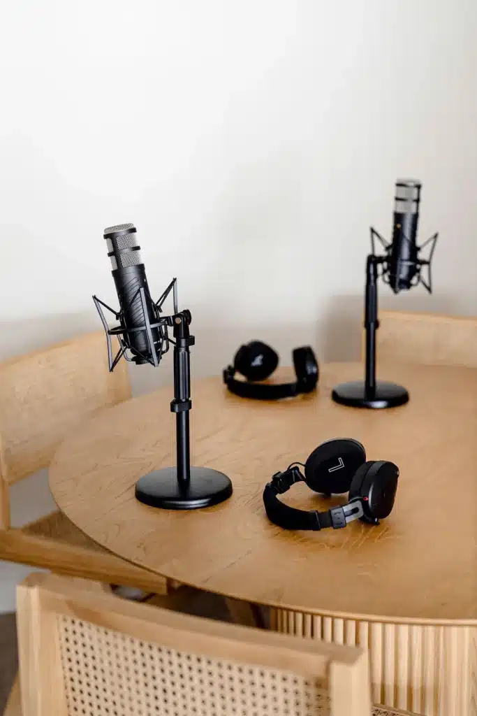Two podcast microphones on desktop stands and headphones set up on a wooden table