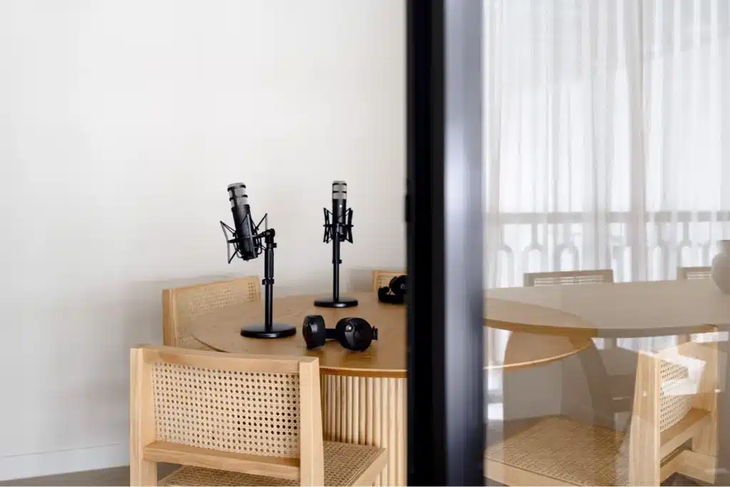 Podcast recording setup with two microphones and headphones on a round wooden table surrounded by woven chairs