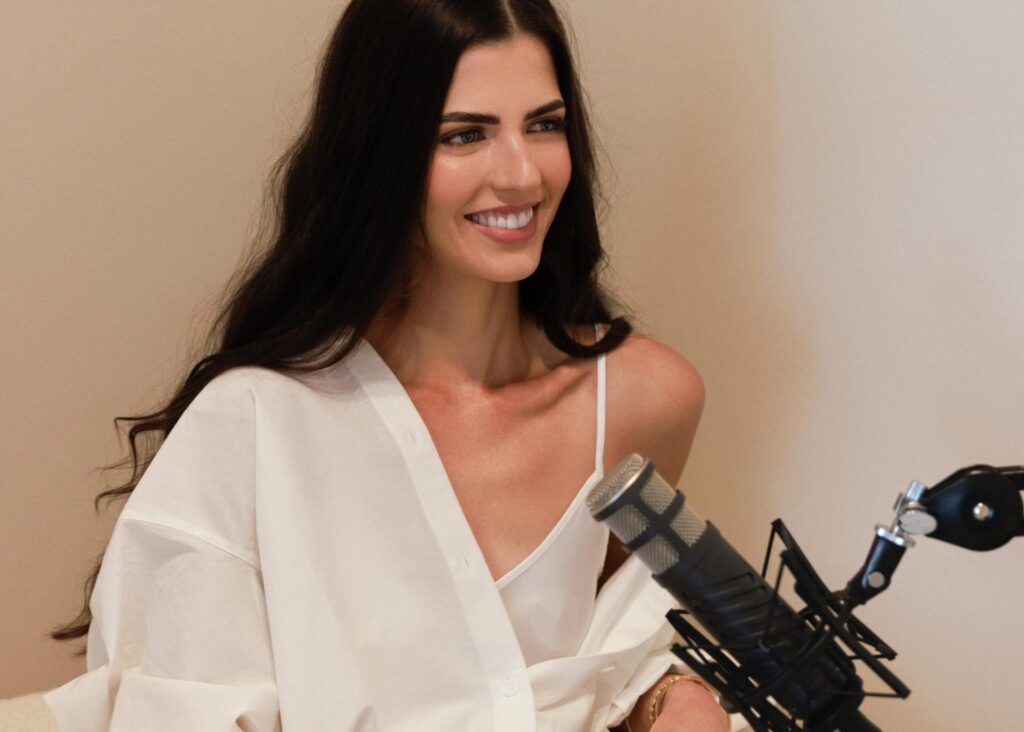 Smiling woman with long dark hair sitting in front of a podcast microphone