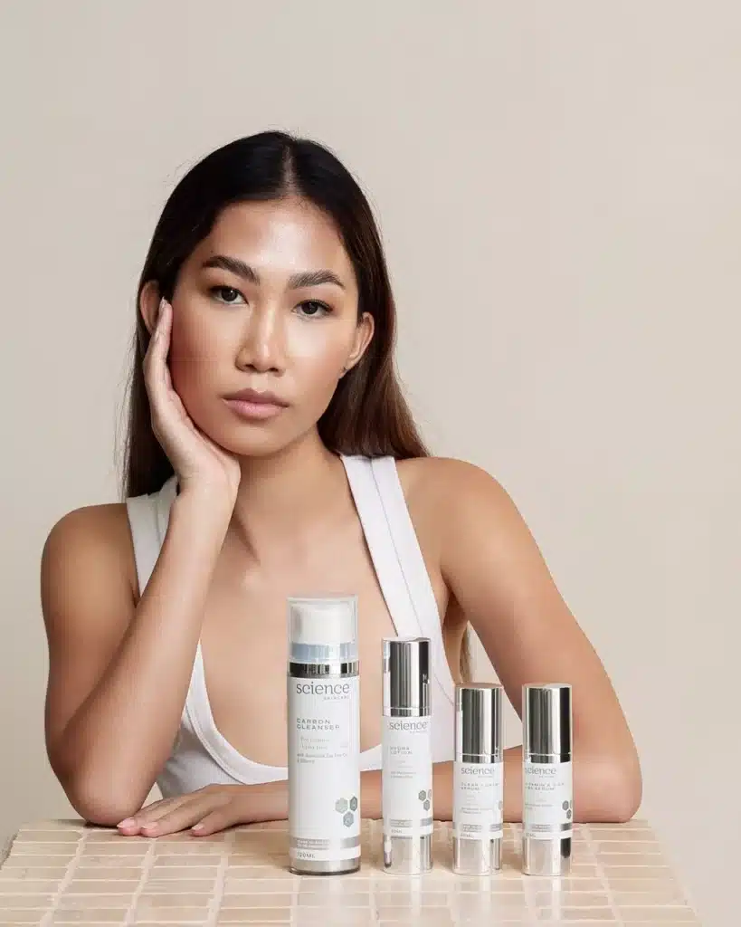 Woman posing behind Science Skincare products including Carbon Cleanser, Hydra Lotion, and serums