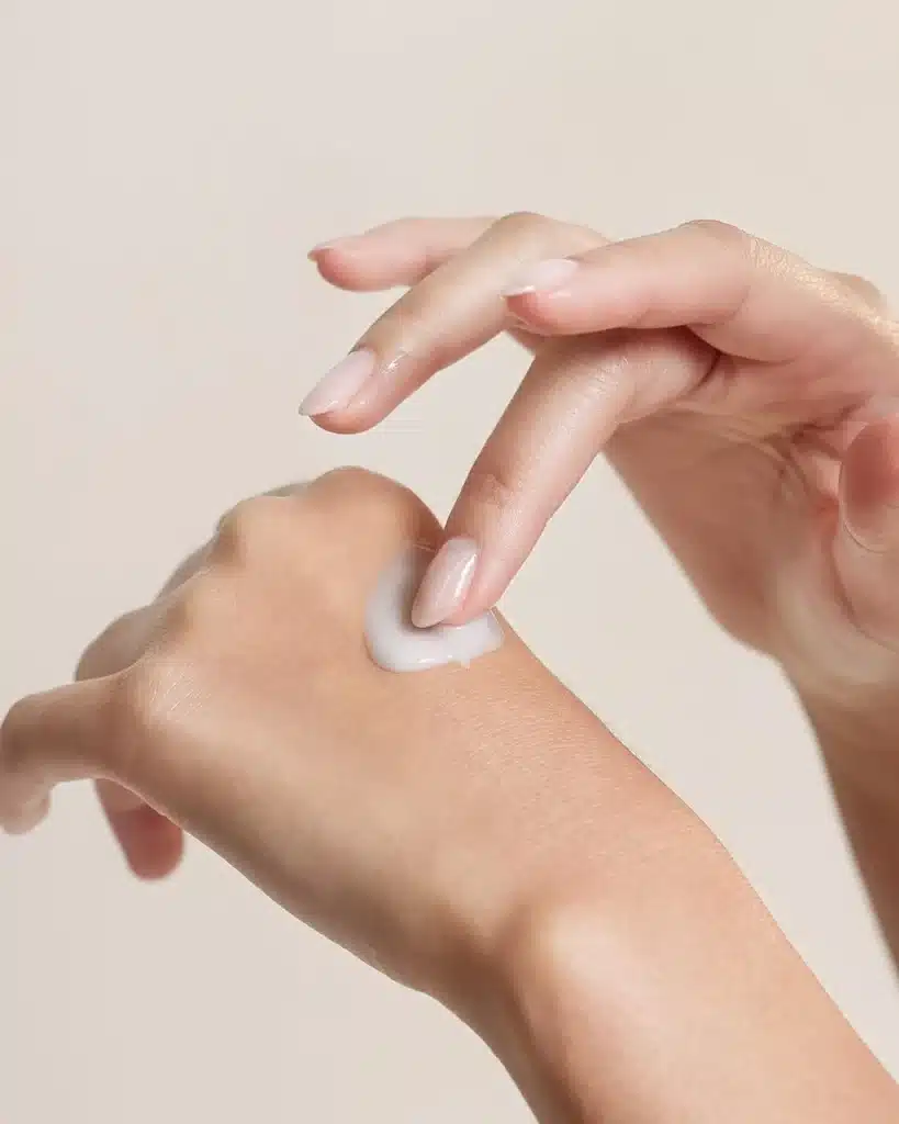 A person dabbing a small amount of white lotion onto the back of their hand