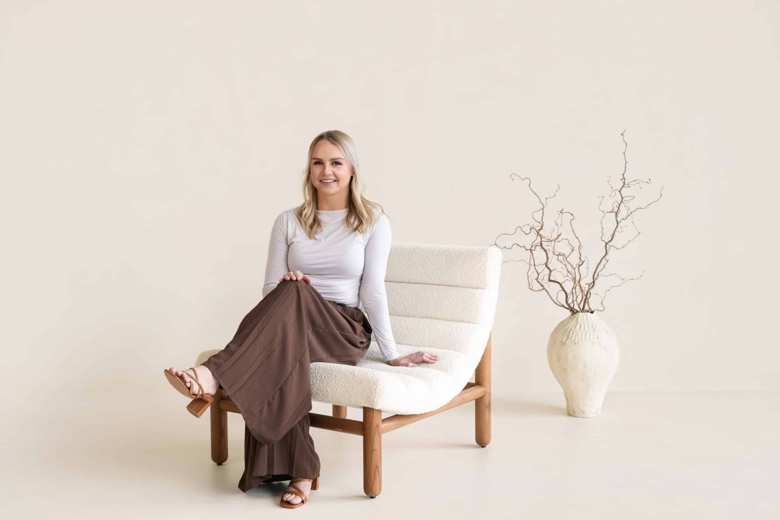 blonge lady sitting in white chair in natural light photography studio for headshots